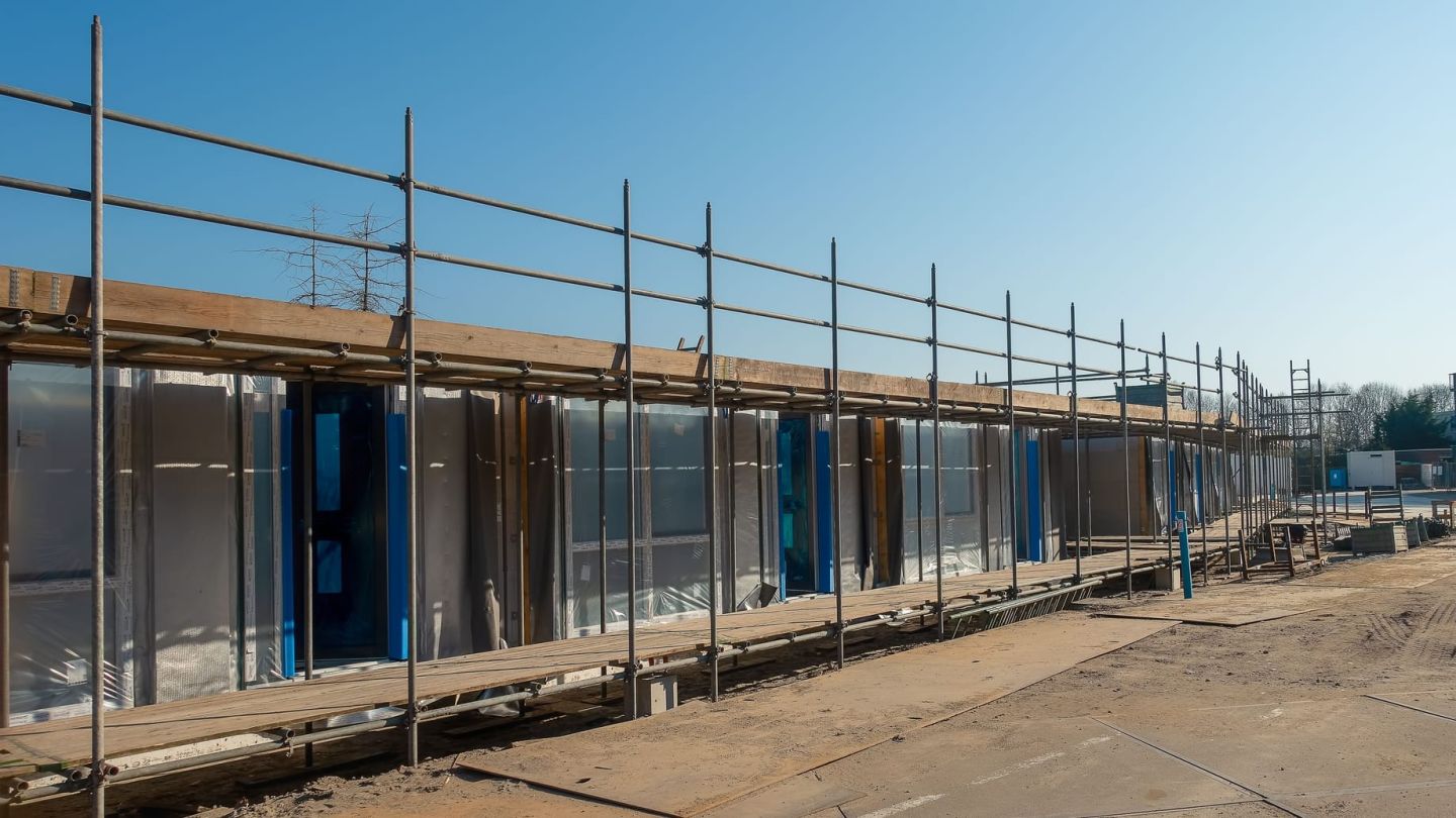 Wohnhausreihe im Rohbau hinter einem Gerüst, die Fassade noch mit Folie verkleidet und offen