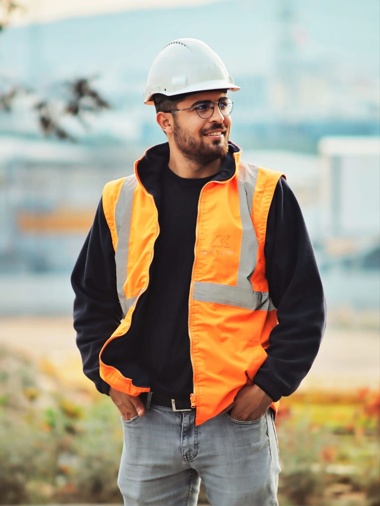 Bauleiter mit Schutzhelm, Schutzbrille und orangefarbener Warnweste steht auf einer Baustelle