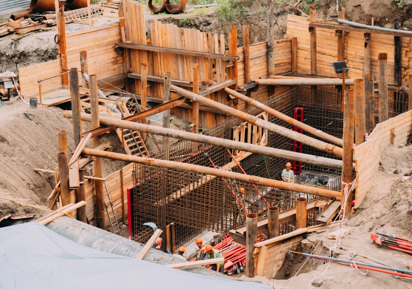 Tiefe Baugrube mit Holzverbau, Aussteifungen und Arbeitern in Warnkleidung auf der Sohle